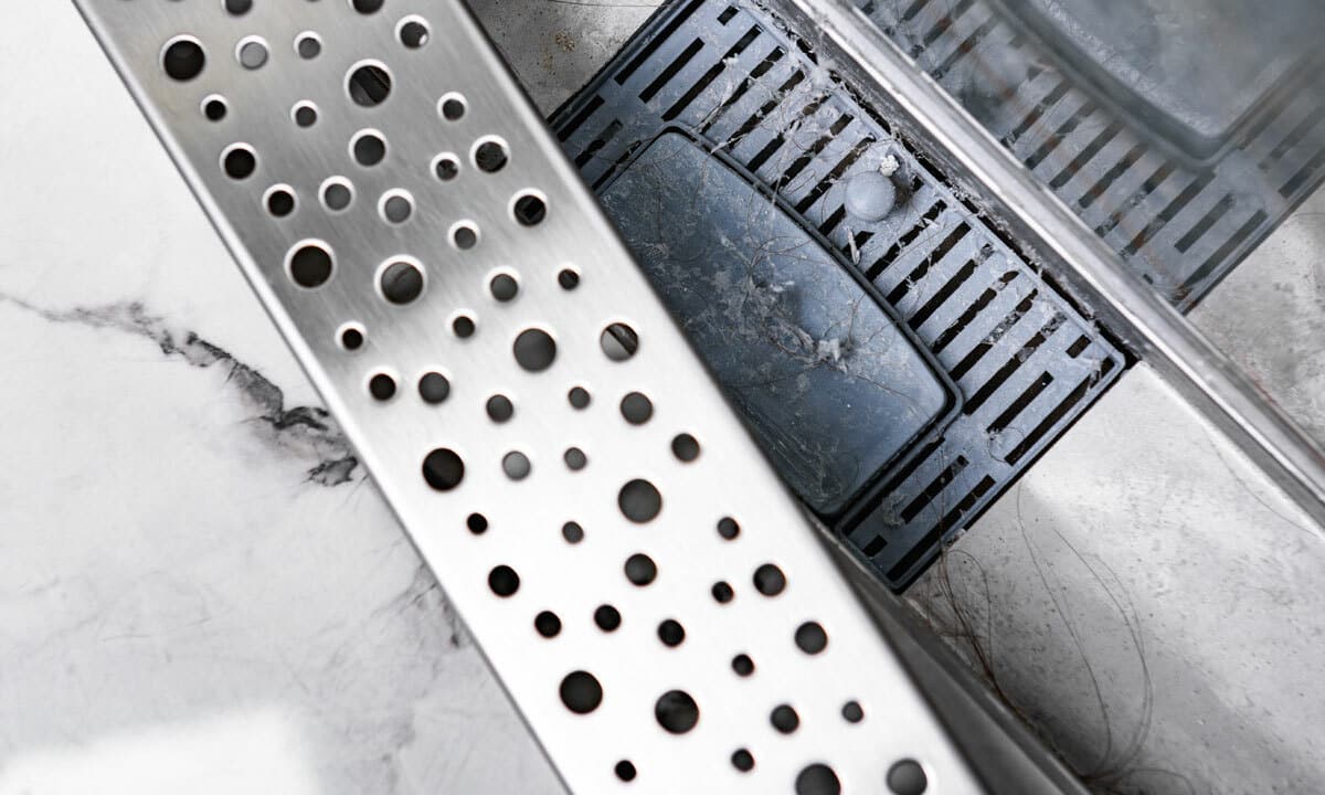 A shower drain exposed to show clogged hair and soap