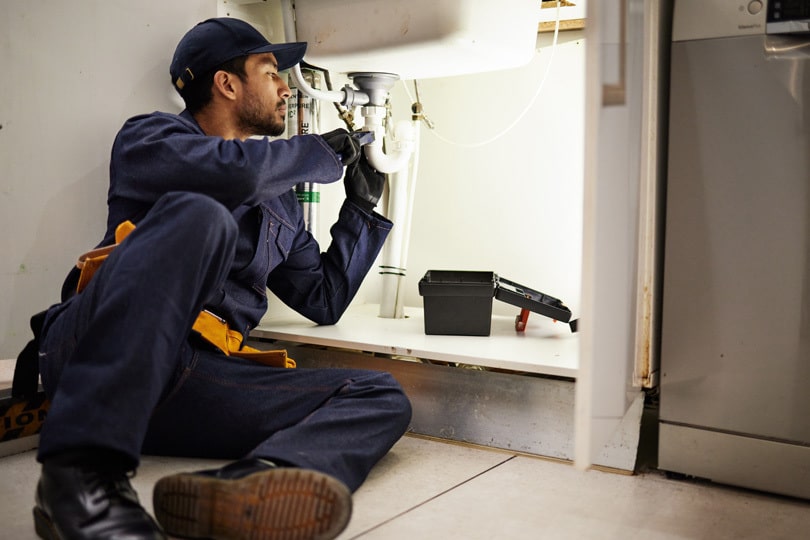 A plumber making adjustments under a sink