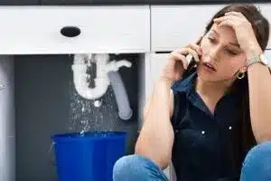 A woman on the phone while the pipes behind her under the sink are dripping