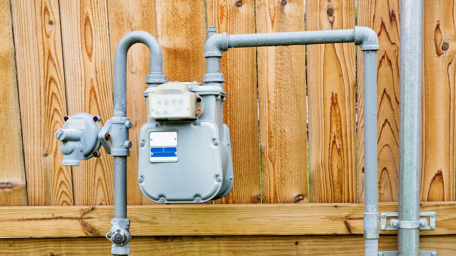 A gas line meter in front of a fence