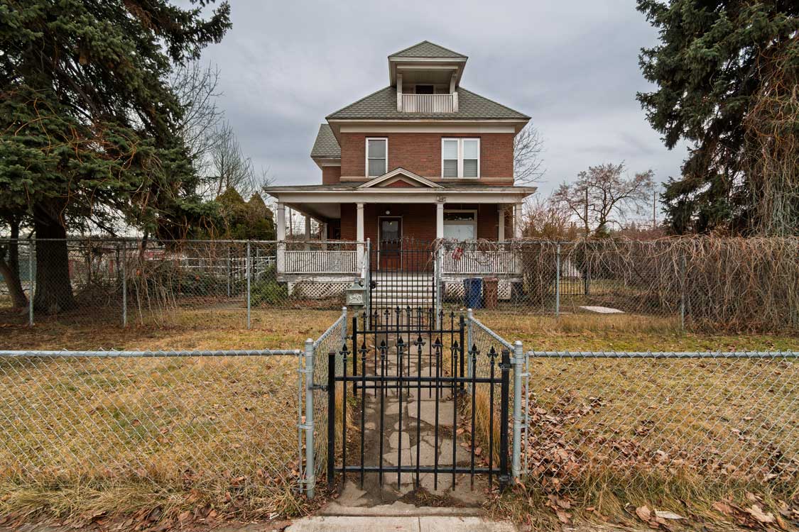 A 19th century large brick Victorian home with multiple fences and covered porch in downtown Spokane, Washington USA.