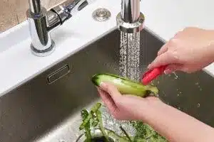 A person peeling cucumbers in the sink