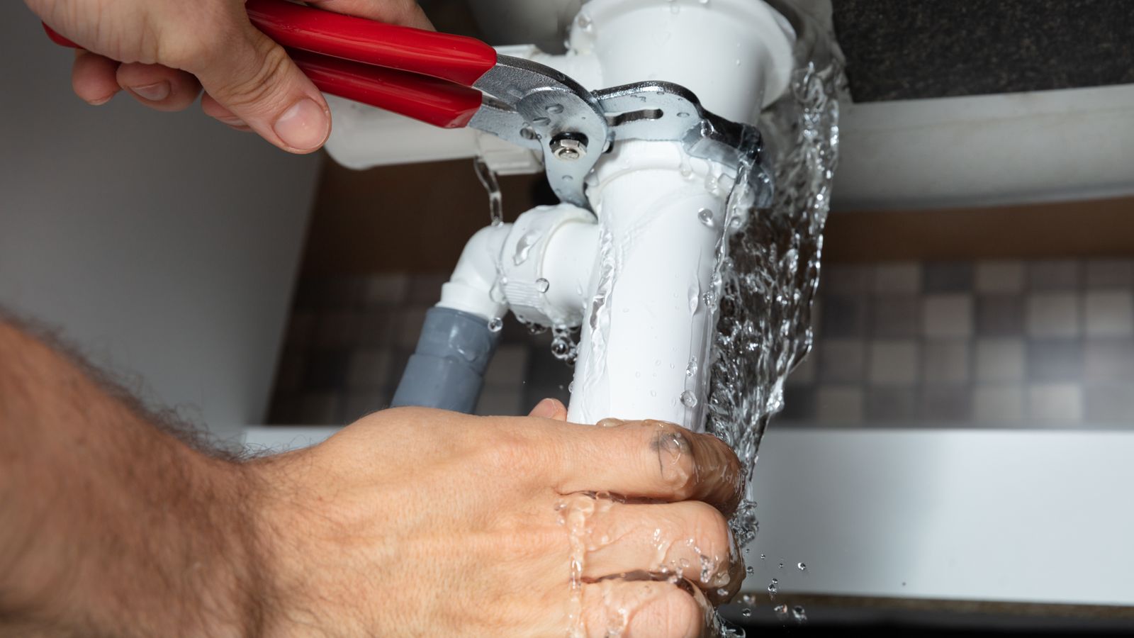 Fixing pipes under a sink while water gushes out everywhere