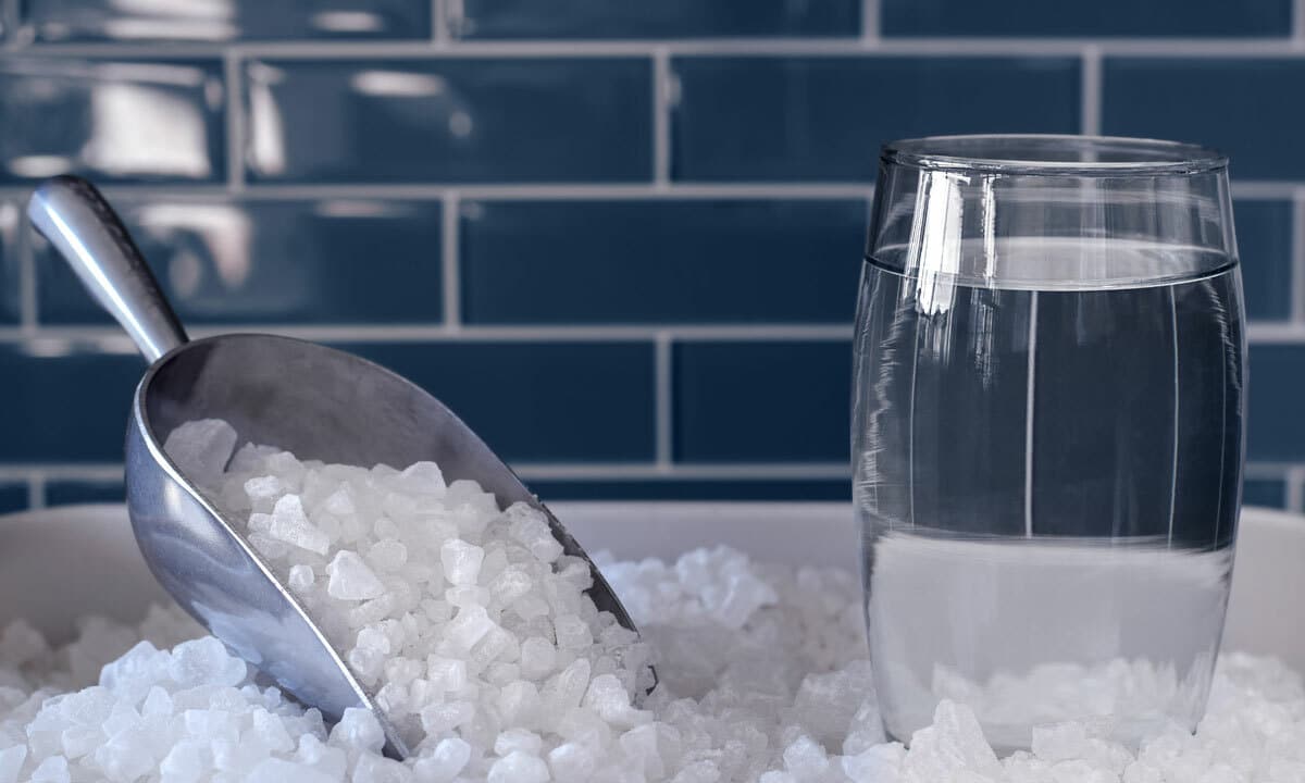 A pile of salt for a water softener next to a clean glass of water